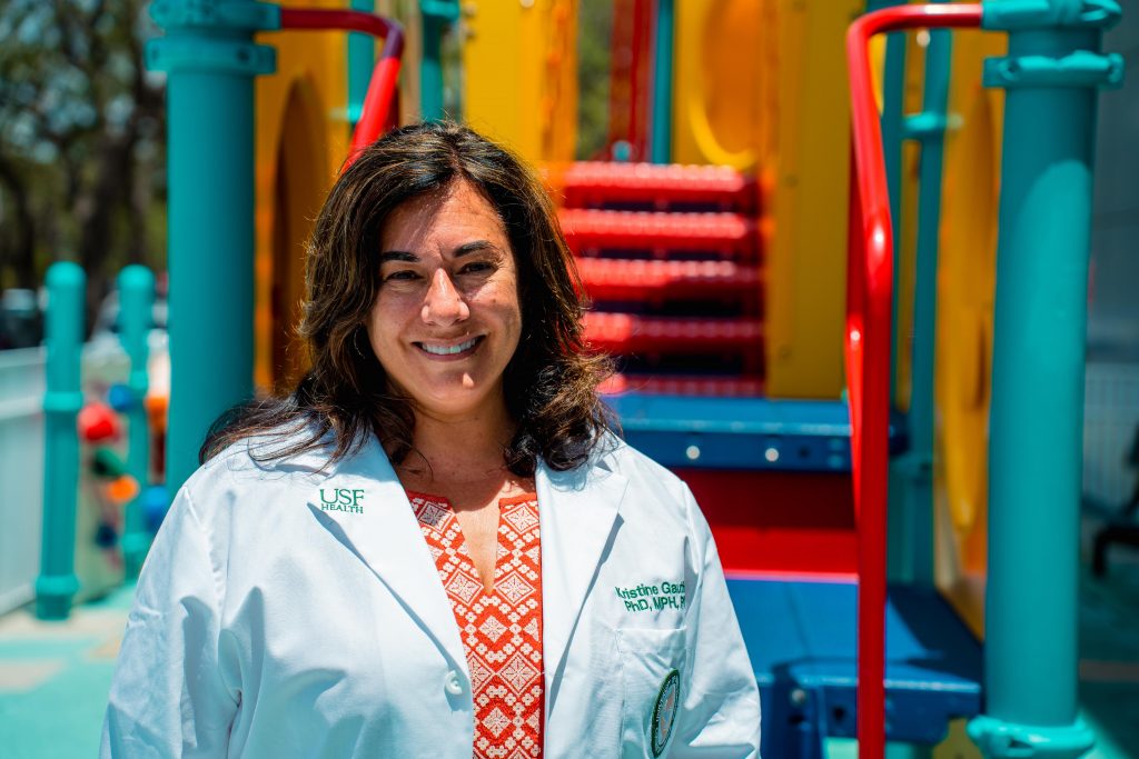 K.Gauthier stands in front of the playground with lab coat on. 