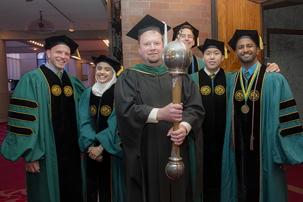 With graduating students is Dr. Michael Schoenberg, president of the MCOM Faculty, who carried the College's Mace.